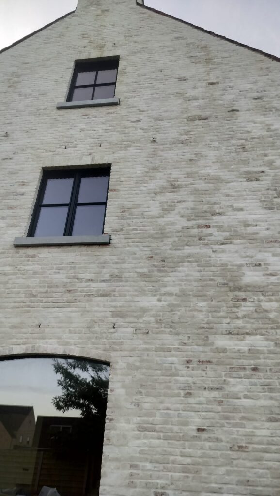 Lichtgrijs gekaleide bakstenen gevel met zwarte ramen